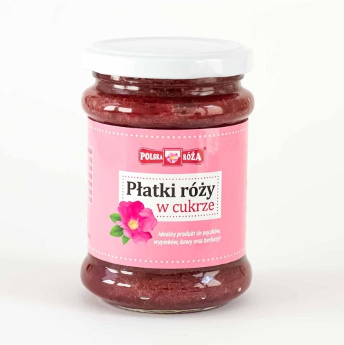 Szklany słoik z ciemnoczerwonymi „Płatkami róży w cukrze” i białą zakrętką o pojemności 320g. Etykieta w kolorze różowym z ilustracją kwiatu róży.
